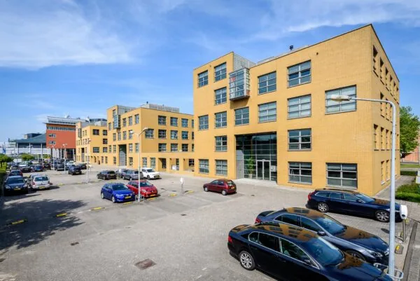 Kantoorpand aan de Rivium 3e Straat met een parkeerterrein op de voorgrond op een zonnige dag.